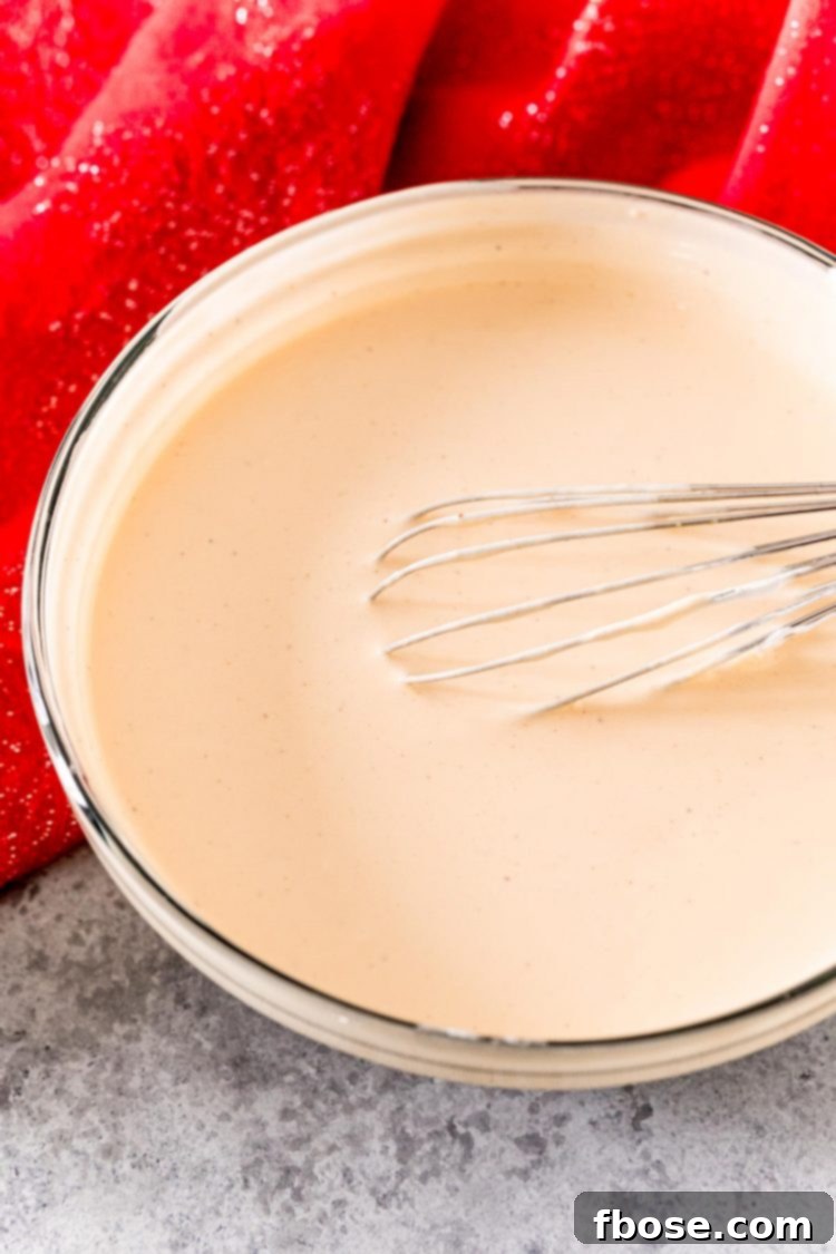 A glass mixing bowl with the eggnog pudding shot mixture being whisked, showing a creamy, smooth consistency.