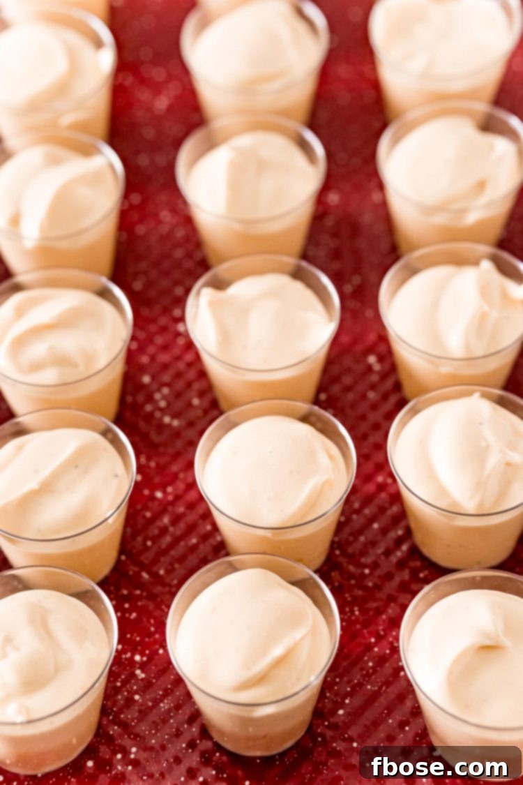 Eggnog pudding shots in small plastic shot glasses, arranged neatly on a red baking sheet.
