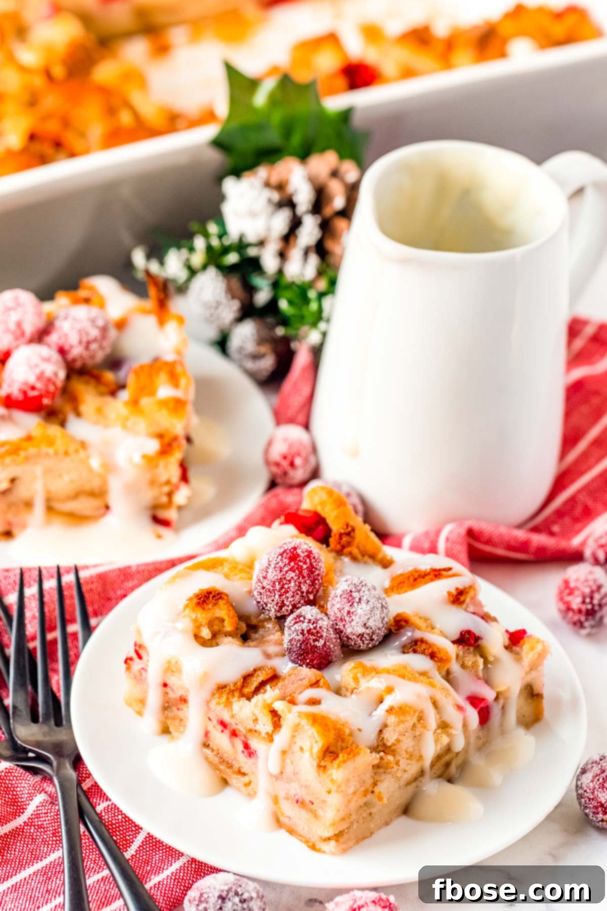 Close up photo of cranberry white chocolate bread pudding on a white plate, showcasing a generous portion ready to be enjoyed.
