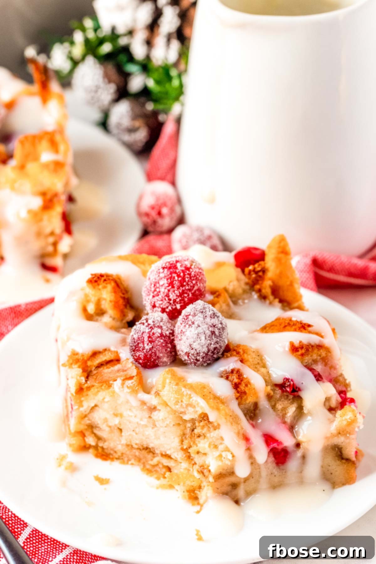 Close up photo of a slice of bread pudding on a white plate with a bite taken out of it, showing the soft interior and inclusions.