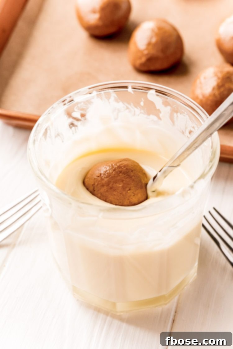 A gingerbread ball being carefully dipped into a bowl of melted white chocolate, illustrating the coating process.