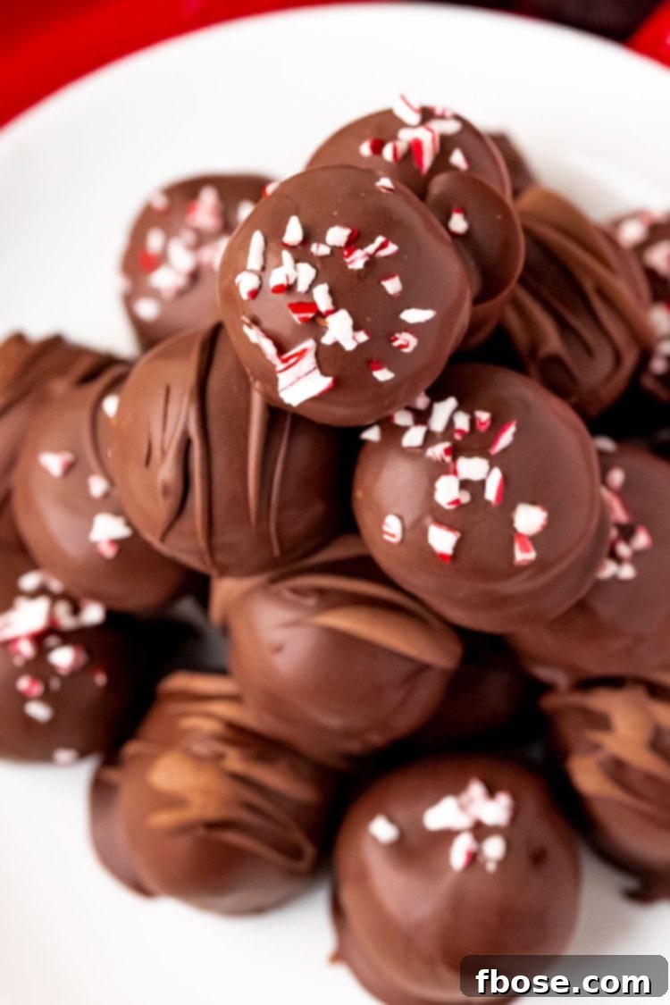 Close up photo of peppermint oreo truffles on a white plate, showcasing their festive appeal and smooth chocolate coating.