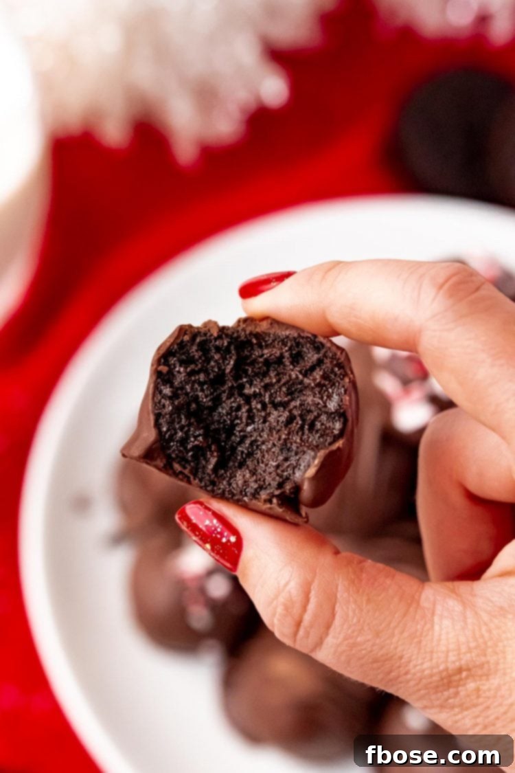 A woman's hand gently holds a Peppermint Oreo Ball, with a small bite taken out, presenting it towards the camera to showcase its delightful interior.