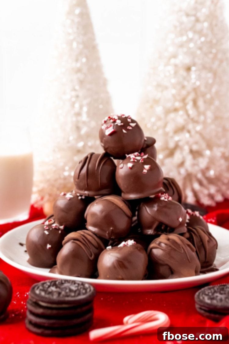 A charming pile of Peppermint Oreo Balls arranged artfully on a white plate, surrounded by elegant holiday decorations.