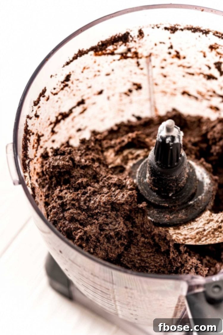 A smooth, dark chocolate truffle mixture actively blending in a food processor, highlighting its thick and sticky texture.