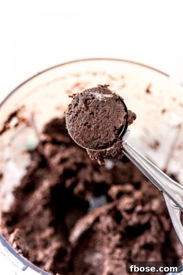 A medium cookie scoop holding a portion of the thick, dark Oreo ball mixture, ready to be rolled into a truffle.