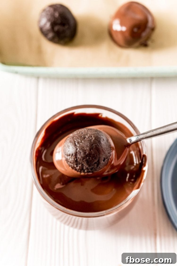 A spoon delicately dipping an Oreo ball into a bowl of melted chocolate, illustrating the coating process.
