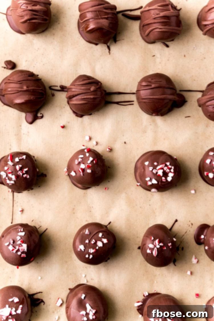 An overhead view of freshly dipped Peppermint Oreo Balls adorned with festive sprinkles, neatly arranged on a parchment-lined baking sheet.