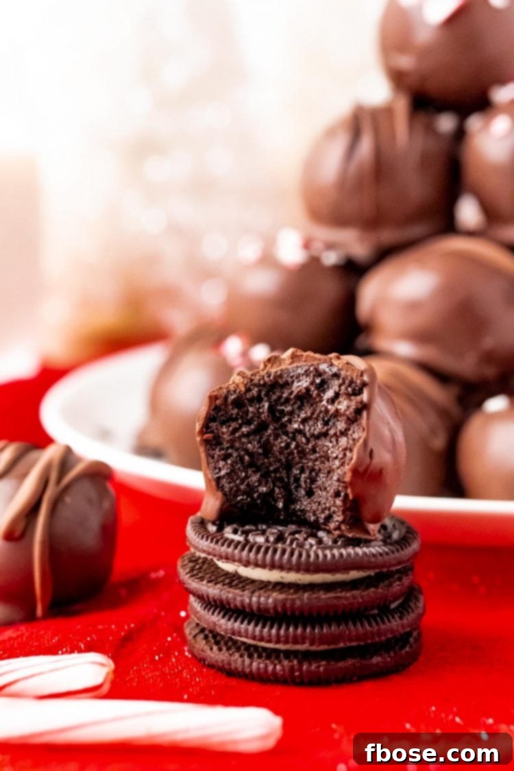 Close up photo of an exquisite Peppermint Oreo Ball resting on a stack of two Oreos, with a generous plate of additional balls blurred in the background, creating a mouth-watering scene.