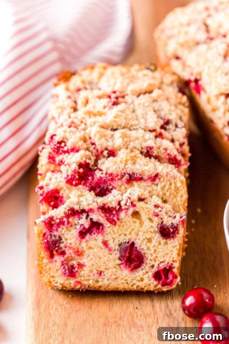 Close up photo of slices of cranberry bread resting on each other on a wooden cutting board.