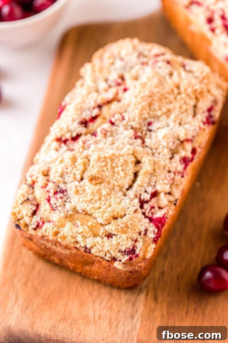 Close up photo of a loaf of cranberry quick bread on a wooden cutting board.