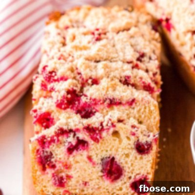 Close up photo of slices of cranberry bread resting on each other on a wooden cutting board.