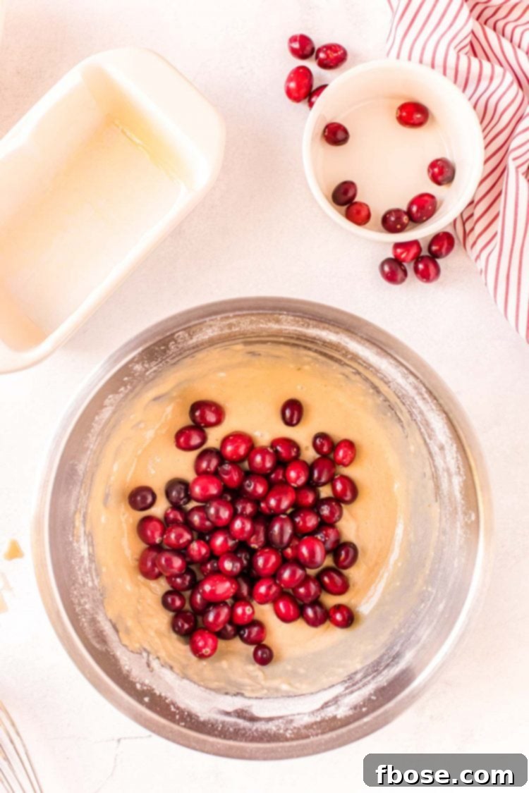 Cranberries being folded into batter in a metal mixing bowl.