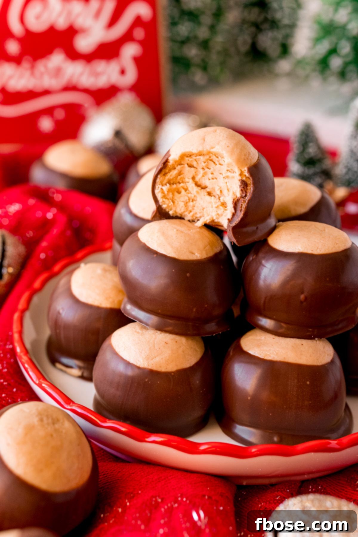 Close up photo of a plate of peanut butter buckeyes, with one featuring a bite taken out, surrounded by charming holiday decorations.