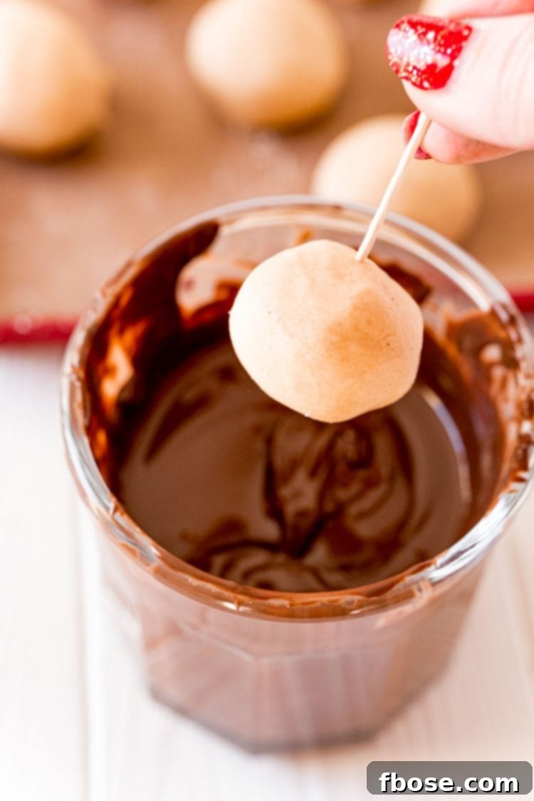 A perfectly rolled peanut butter ball skewered on a toothpick, poised above a bowl of melted chocolate, ready for dipping.