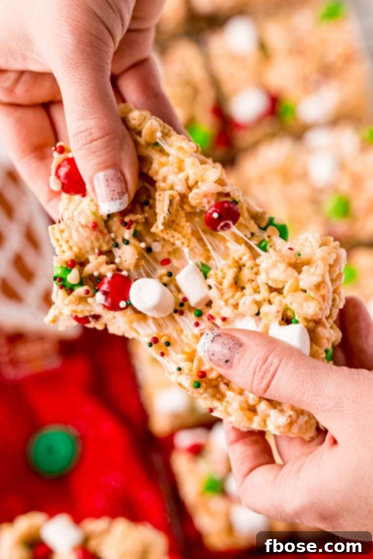 A woman's hand gently pulling apart a gooey Christmas rice krispie treat, showing its soft and chewy interior.