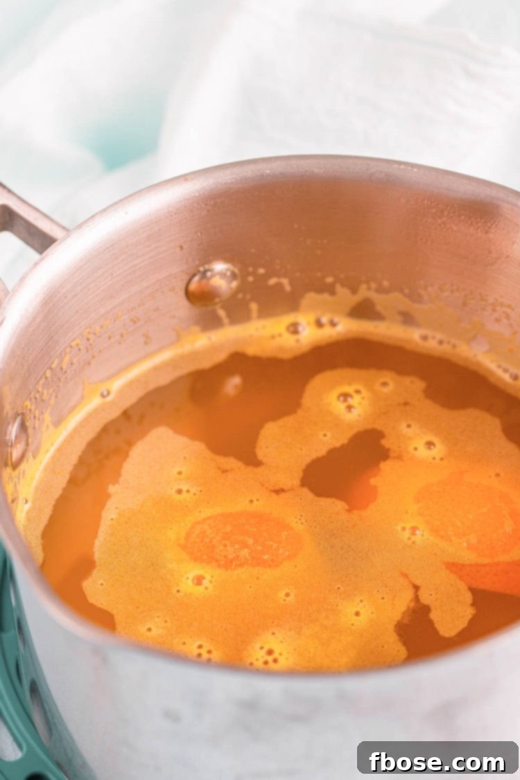 Orange simple syrup simmering gently in a small saucepan on a stove, infusing with flavor.