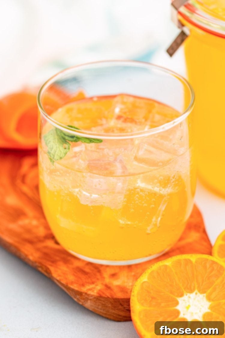 A glass filled with ice and vibrant orange simple syrup, garnished with an orange slice, ready to be mixed into a drink.