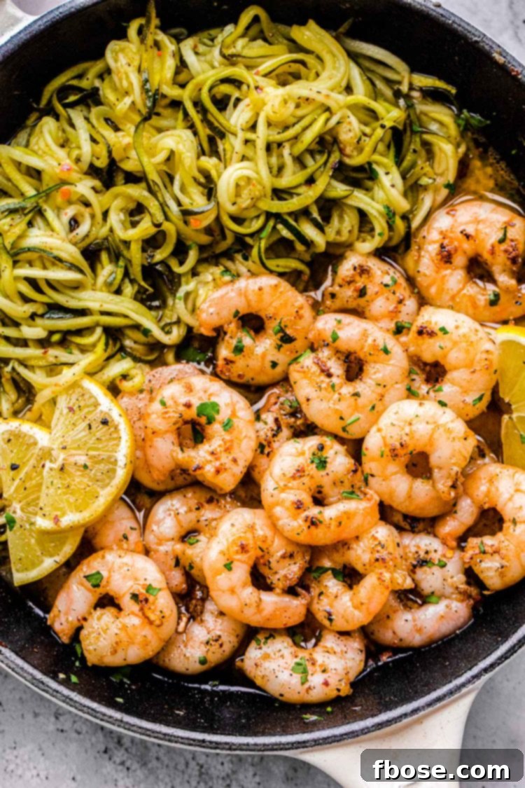 Close up photo of lemon garlic shrimp in a skillet with zucchini noodles and lemon wedges, garnished with fresh parsley.