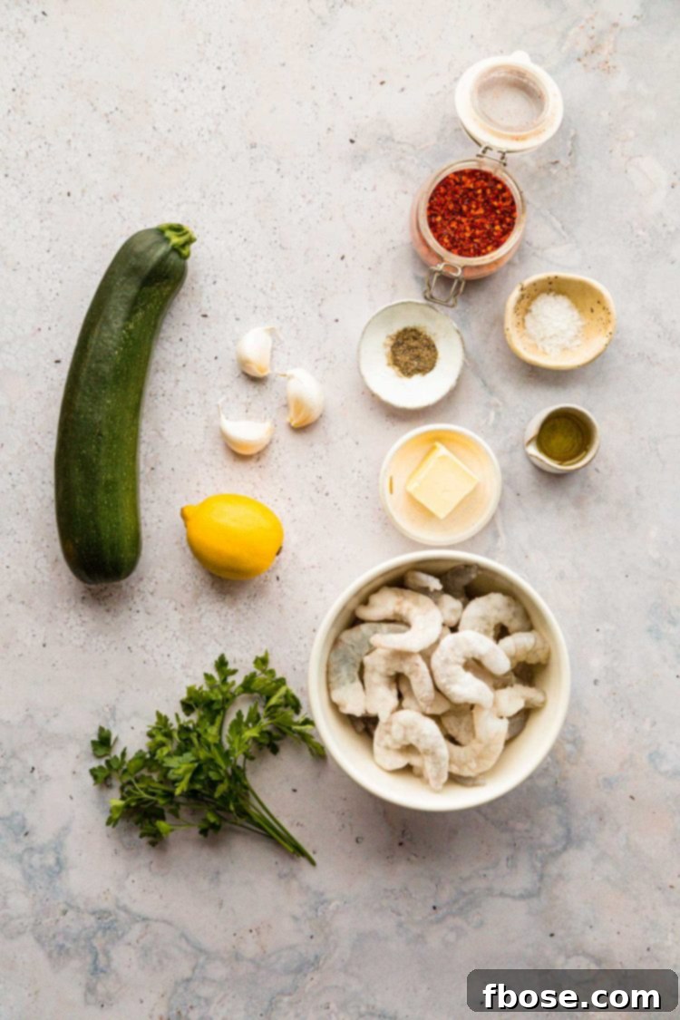 Overhead photo of fresh ingredients for lemon garlic butter shrimp and zucchini noodles laid out on a grey kitchen counter, including shrimp, zucchini, lemon, garlic, and spices.
