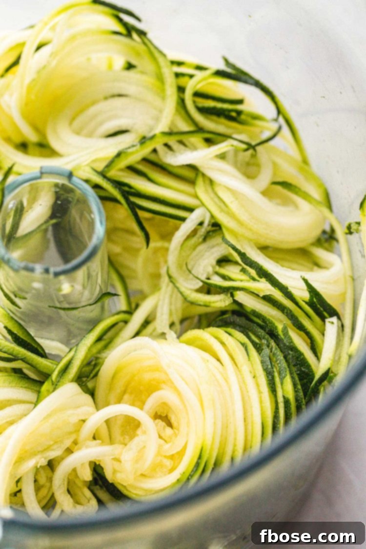 Close up photo of zucchini being spiralized into noodles using a spiralizing tool.