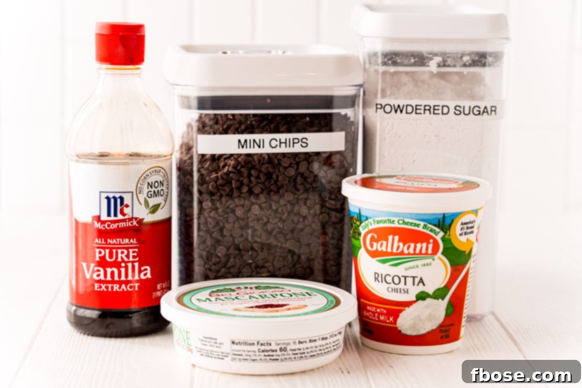 Various ingredients like ricotta, mascarpone, powdered sugar, vanilla extract, and mini chocolate chips laid out on a clean white surface, ready for making cannoli dip.