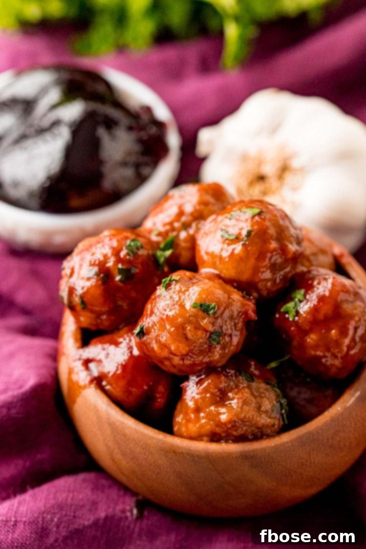Close up photo of grape jelly meatballs in a brown bowl, garnished with fresh parsley.