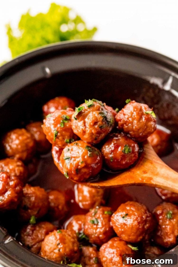 A wooden spoon scooping savory grape jelly meatballs out of a slow cooker, ready to serve.