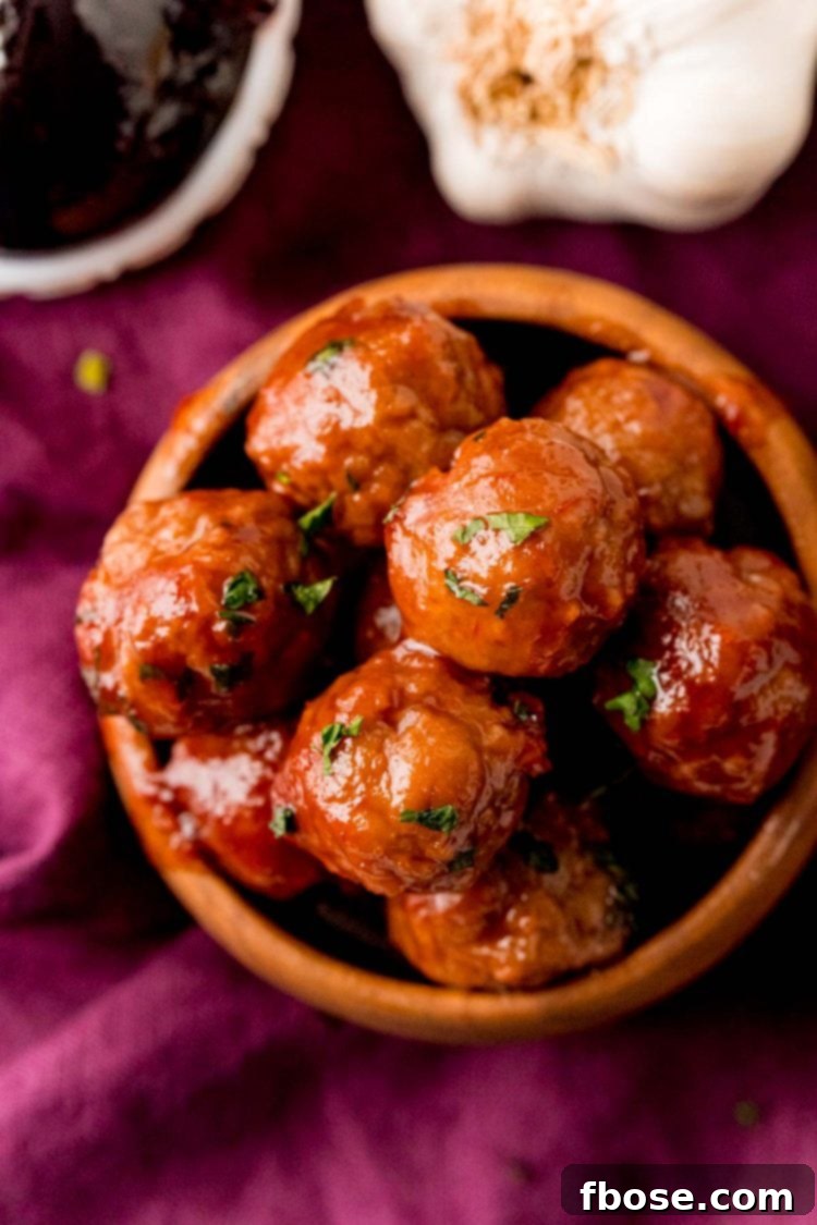 Close up photo of grape jelly meatballs in a wooden bowl on a purple napkin, ready for serving.
