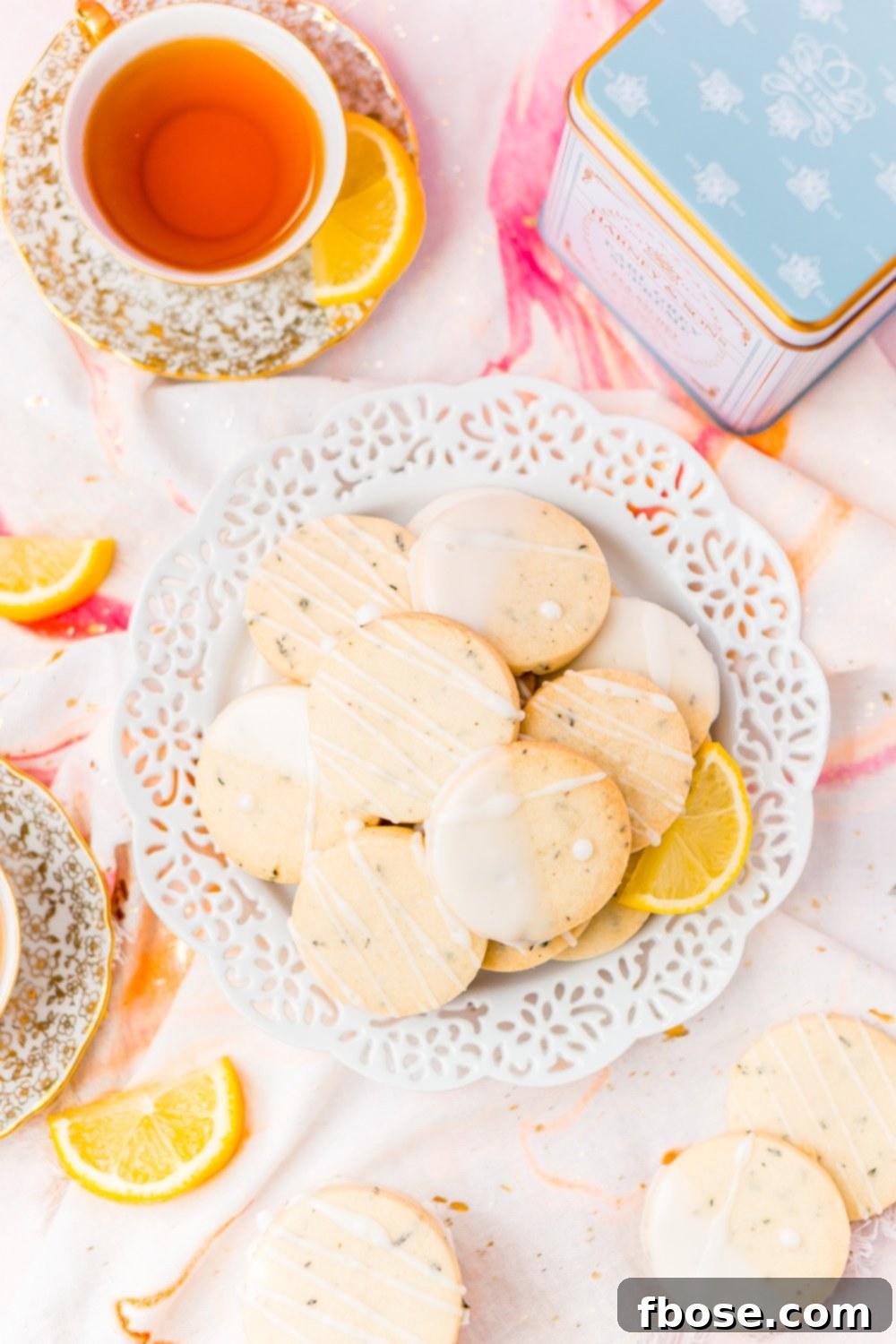 A white plate generously filled with golden Earl Grey Shortbread Cookies, accompanied by cups of tea and fresh lemon slices, inviting a cozy tea time moment.
