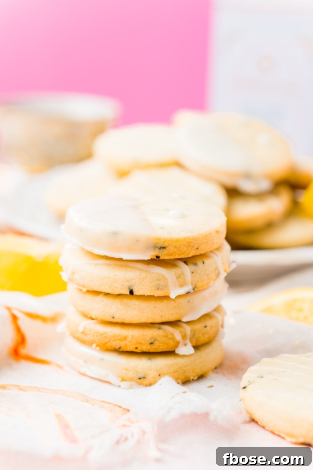 A stack of five Earl Grey Shortbread Cookies, beautifully adorned with a zesty lemon glaze, with more cookies casually arranged on a plate in the soft focus background.