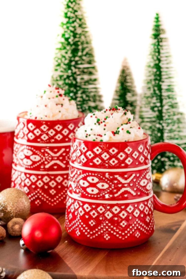 A vibrant red mug filled with Eggnog Hot Chocolate, beautifully topped with a swirl of whipped cream and festive Christmas sprinkles.