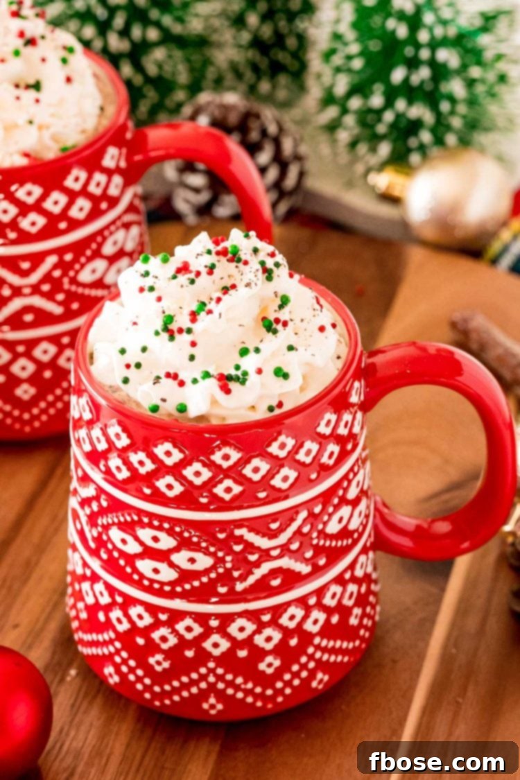 A close-up shot of a charming red Christmas mug, brimming with luscious Eggnog Hot Chocolate, adorned with a generous topping of whipped cream and colorful sprinkles.