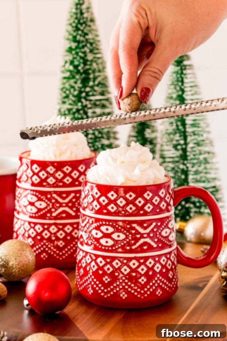 A woman's hand gracefully grates fresh nutmeg over a steaming mug of Eggnog Hot Chocolate, adding a fragrant and authentic touch to the festive drink.