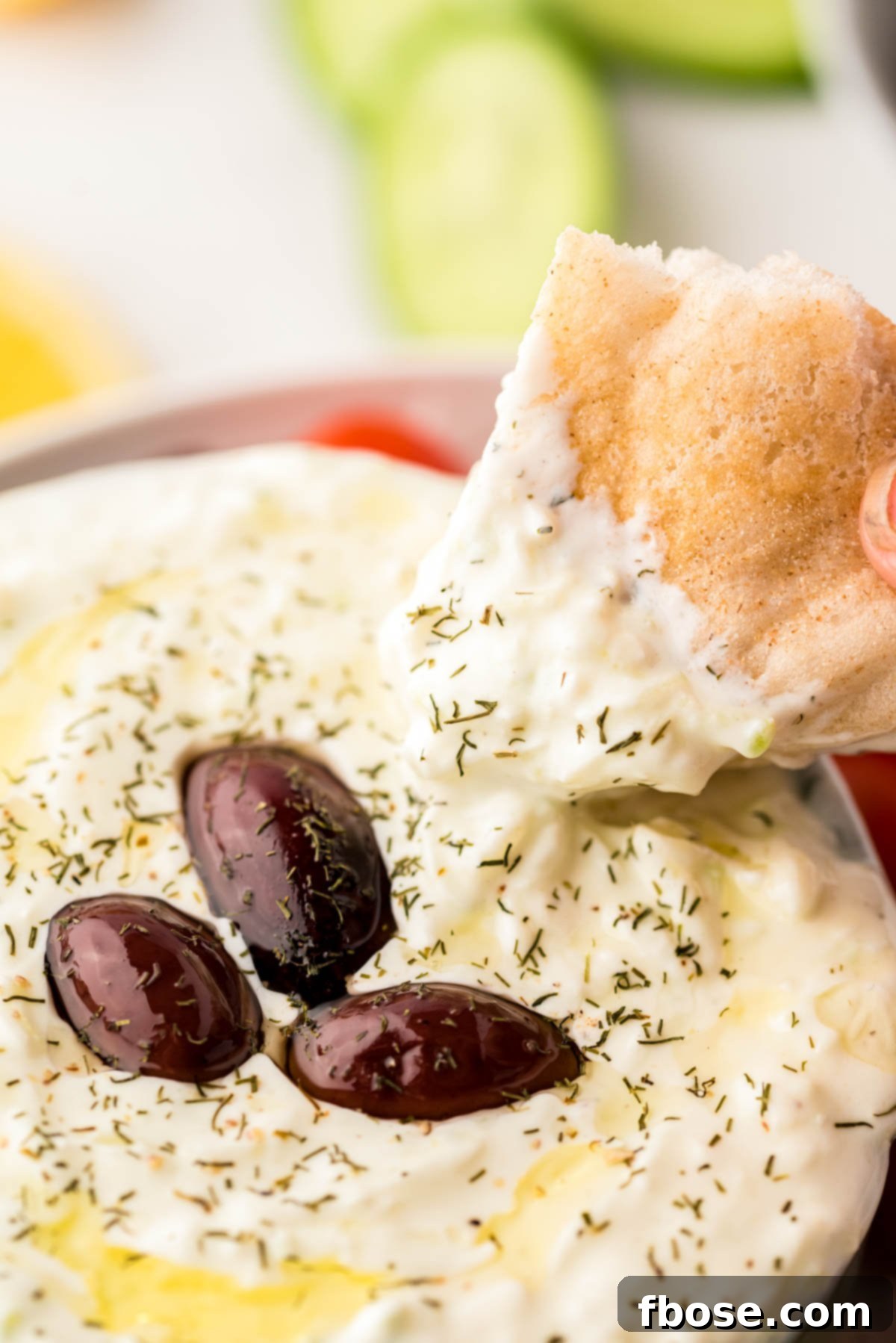 Creamy Greek Cucumber Tzatziki 6 A piece of pita bread being dipped in a bowl of tzatziki sauce.