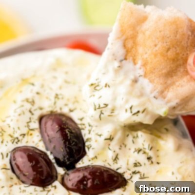 Creamy Greek Cucumber Tzatziki 7 A piece of pita bread being dipped in a bowl of tzatziki sauce.