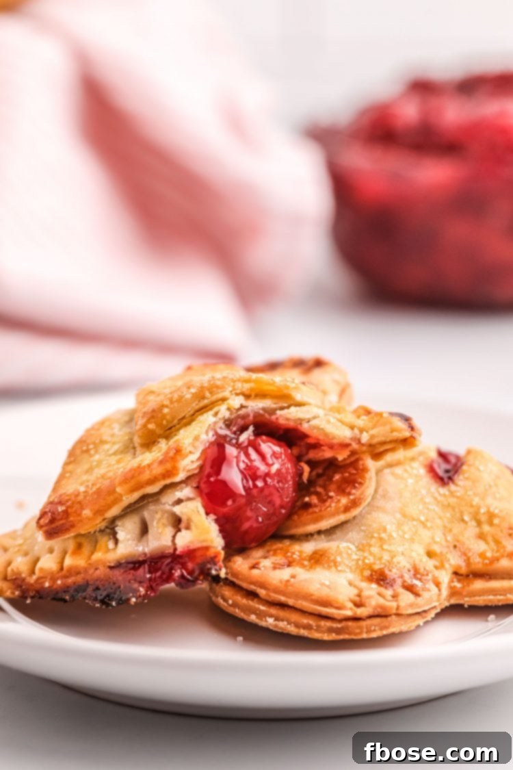 Effortless Cherry Pastry Pockets 4 Close up photo of cherry hand pies on a plate, one has a bite taken out of it.