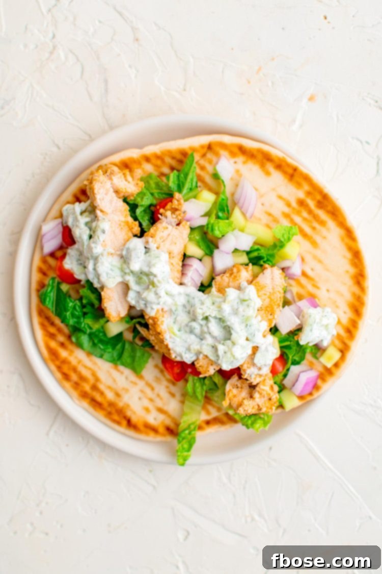 Chicken gyros being assembled on a white plate.