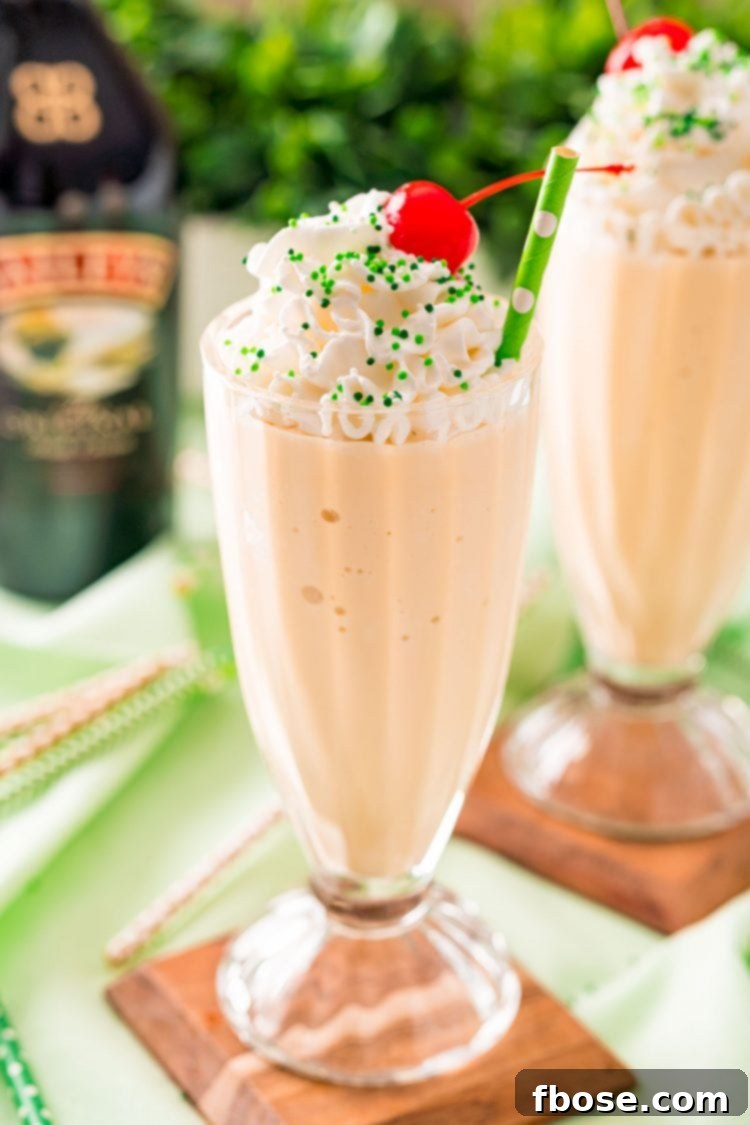 Effortless Irish Cream Indulgence 2 Close up photo of a milkshake glass filled with a Bailey's milkshake and topped with whipped cream and a cherry on a green napkin.