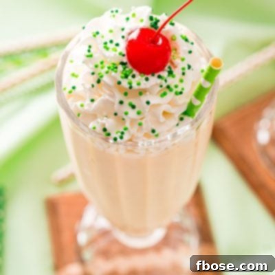 Effortless Irish Cream Indulgence 5 Close up photo of a milkshake glass filled with a Bailey's milkshake and topped with whipped cream and a cherry on a green napkin.
