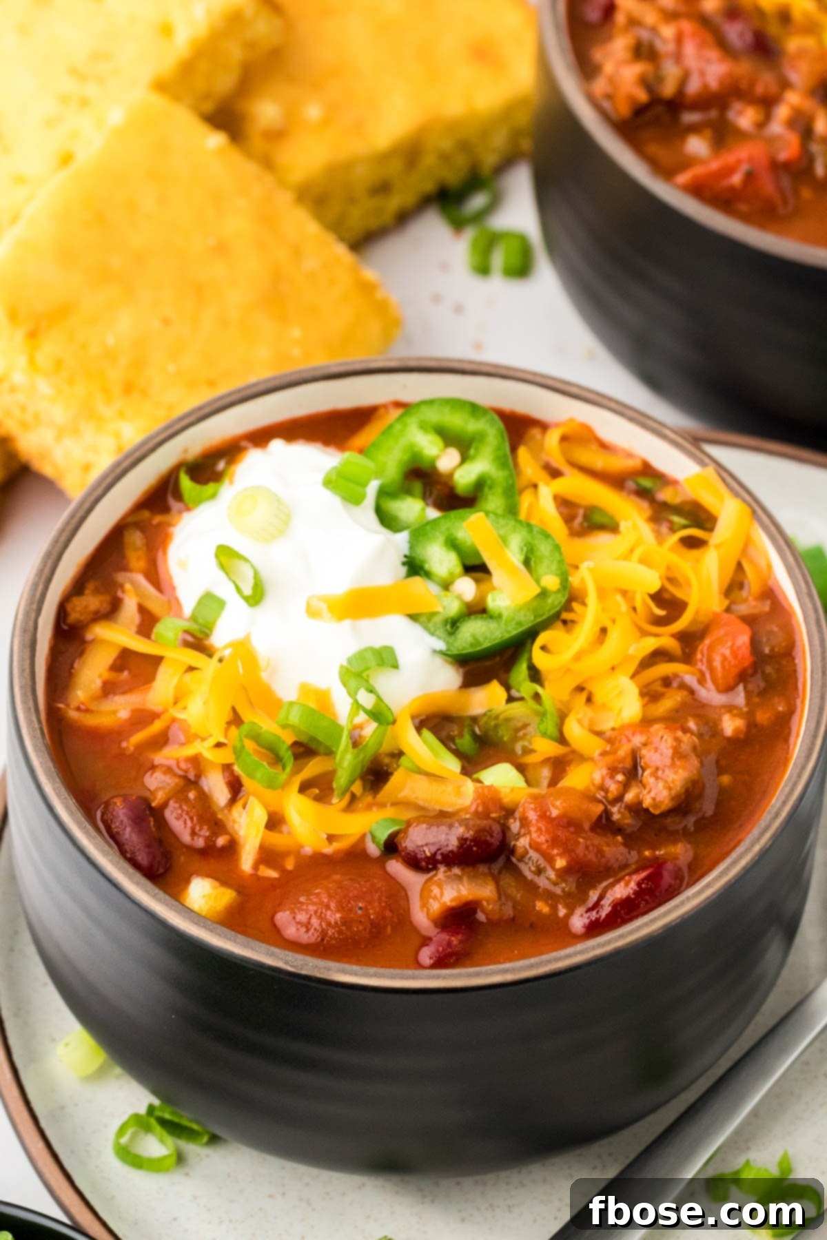 A black bowl filled with turkey chili and topped with sour cream and cheddar, ready to be enjoyed.