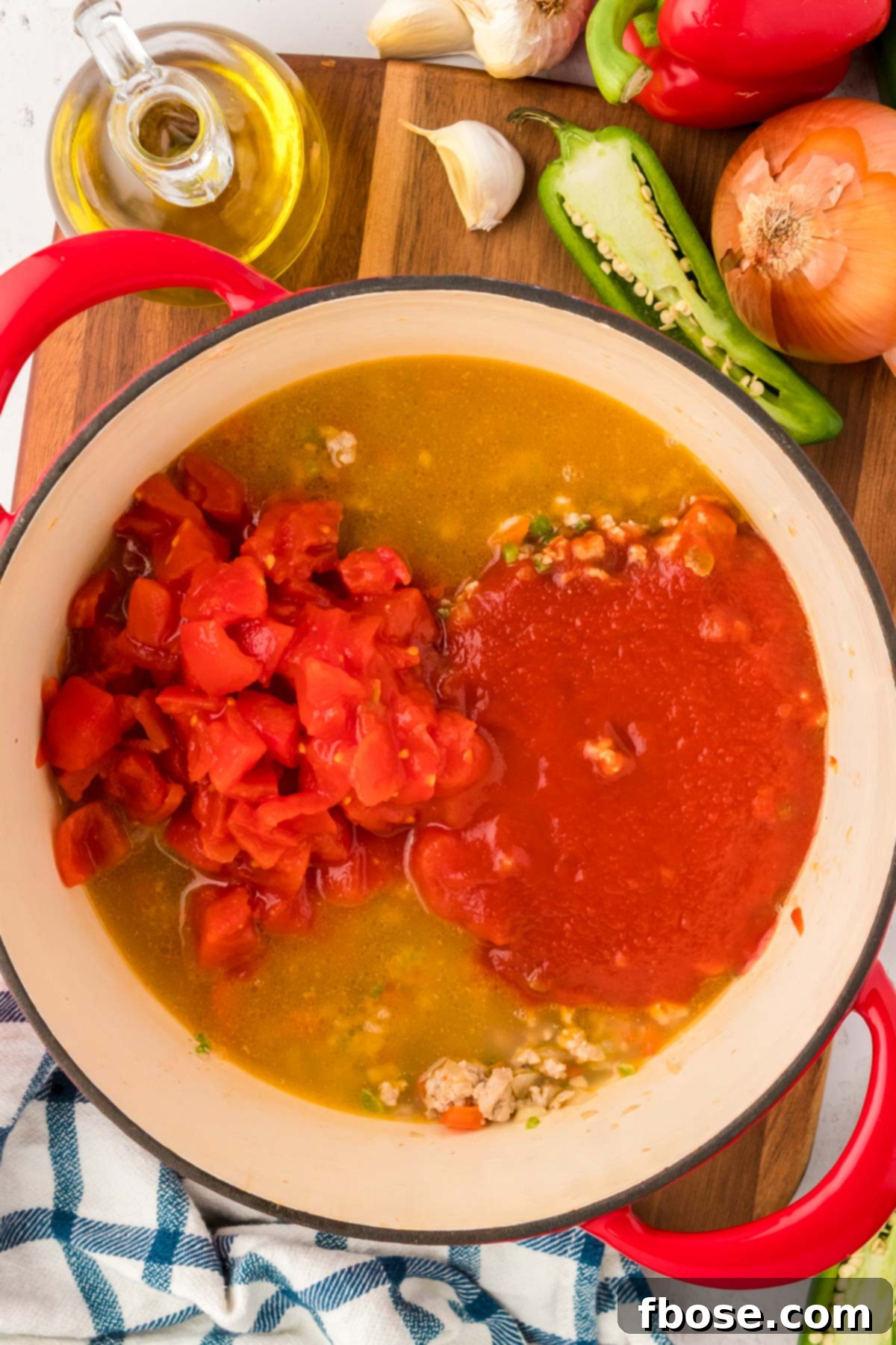 Tomato sauce and diced tomatoes being added to a Dutch oven with chicken stock, ground turkey, and sautéed vegetables.