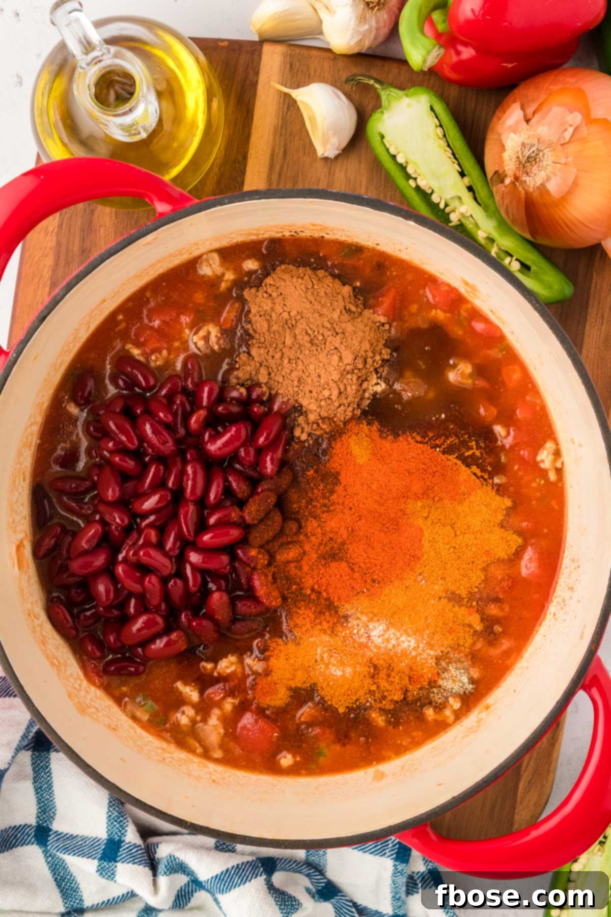 Kidney beans and a variety of spices being added to a Dutch oven to prepare the chili.