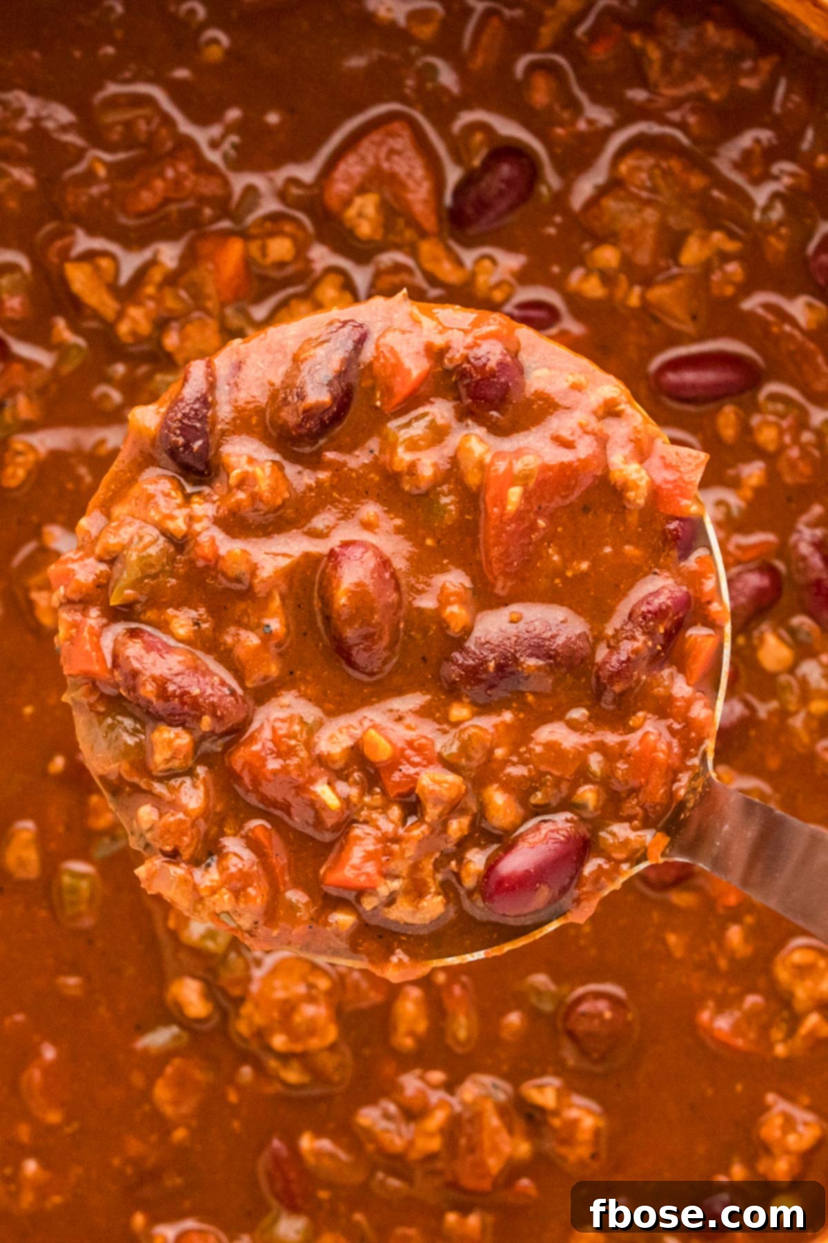 A ladle scooping healthy turkey chili out of a pot, ready to be served.