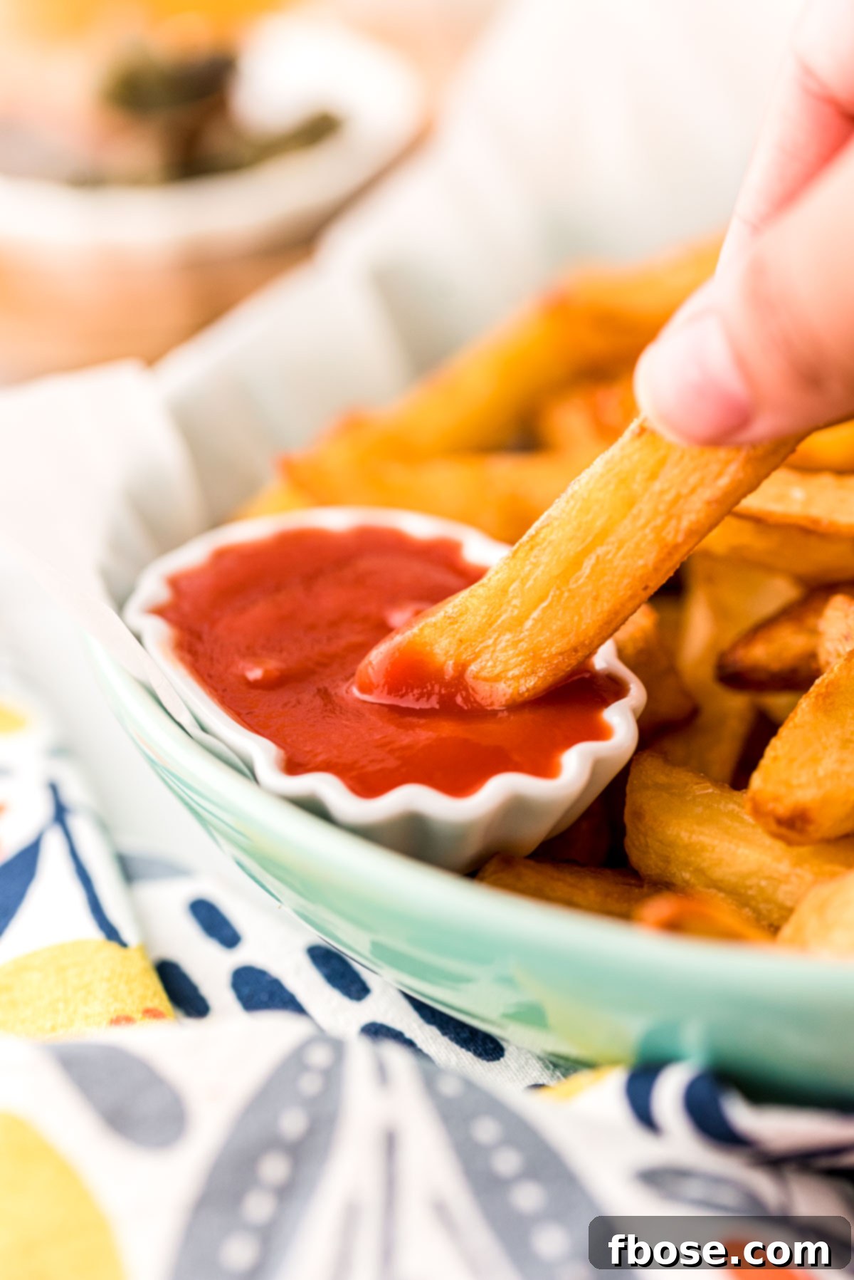 Close up photo of a hand dipping a French fry in a small bowl of ketchup.