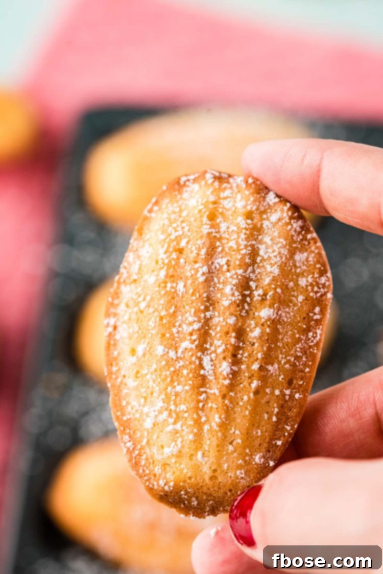 A woman's hand holding a perfect French madeleine, highlighting its golden color and characteristic hump.