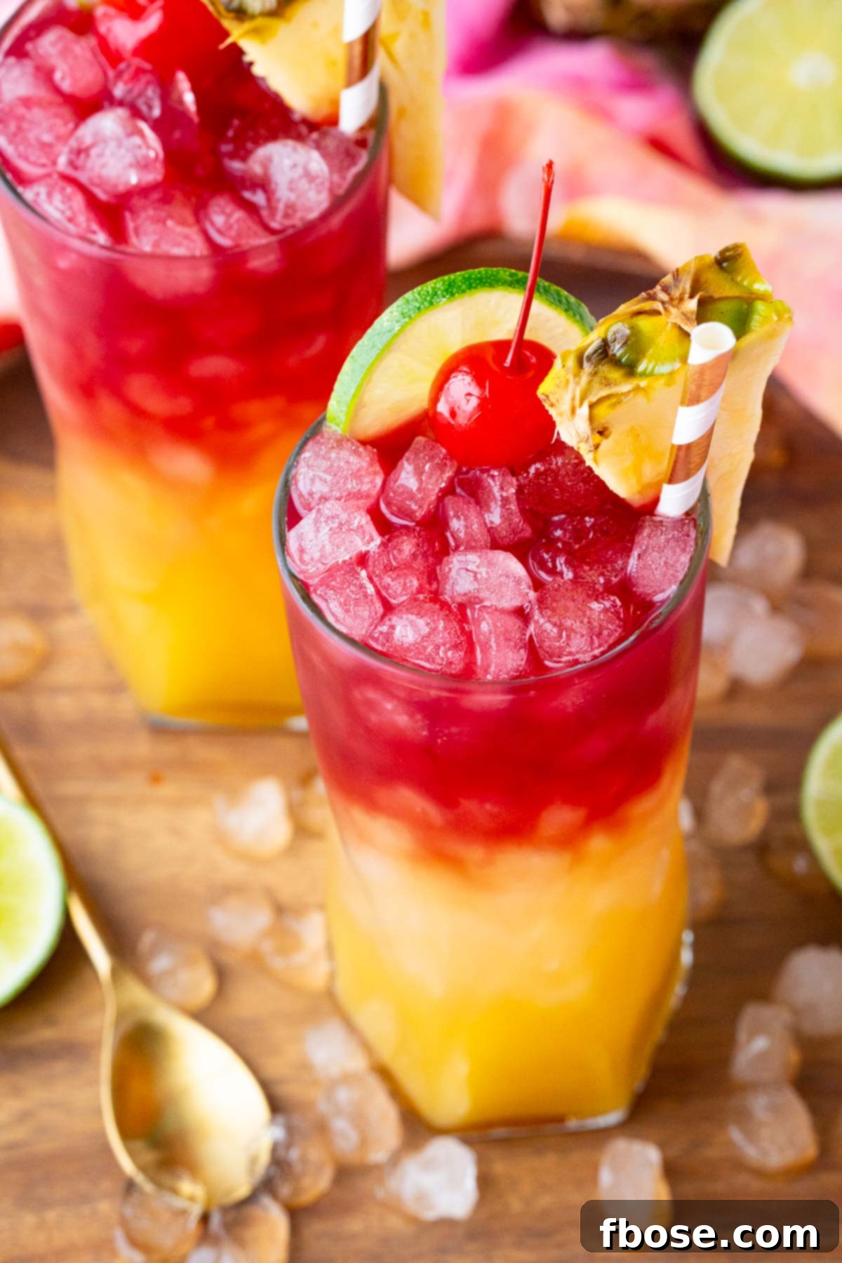 Close up photo of a Malibu Bay Breeze drink garnished with pineapple, cherry, and lime, showcasing the appealing layered colors.