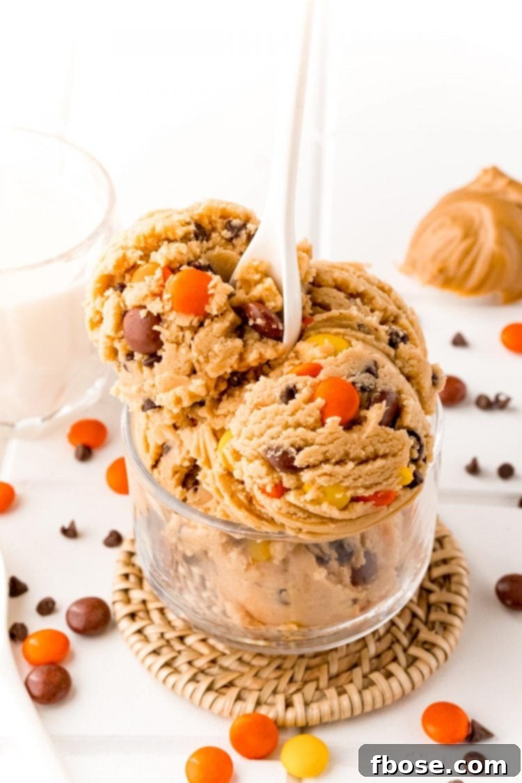 Edible peanut butter cookie dough in a clear glass bowl with a white spoon resting in it.