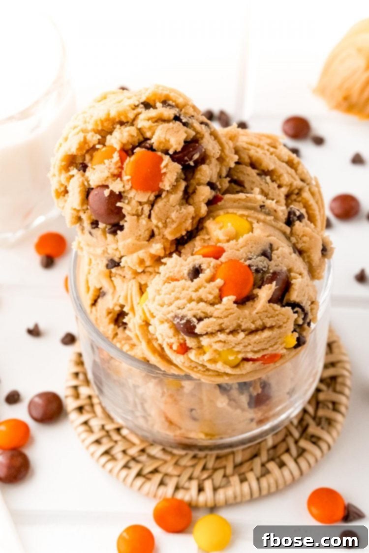 Close up photo of scoops of edible peanut butter cookie dough in a glass bowl on a white table, ready to be enjoyed.