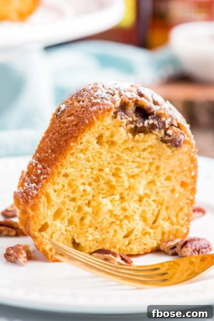 Close up photo of a slice of rum cake on a white plate with a blue napkin in the background.